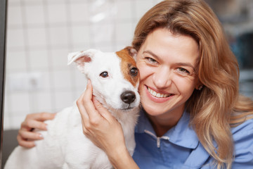 Close up of a happy female vet doctor cuddling with adorable dog. Cute jack russel terrier puppy at veterinary clinic