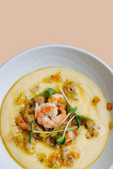 Hot mash soup with shrimp and vegetables in a white plate over pink background