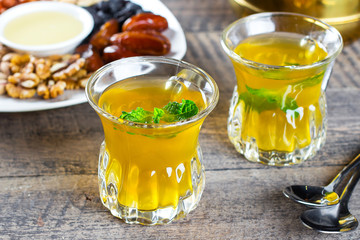 Oriental tea with mint, honey, nuts and dried fruits on wooden table background. Ramadan drink