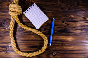 Rope with noose for the suicide, blank notepad and pen on wooden background