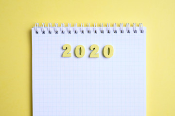 Wooden figures 2020 next to the notebook on a yellow background. Top view.