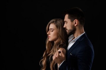 elegant couple on black background. man embracing beautiful woman in black dress. copy space