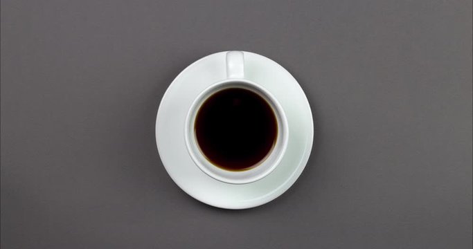 stop motion footage White cup with Black coffee drink is rotating on gray background