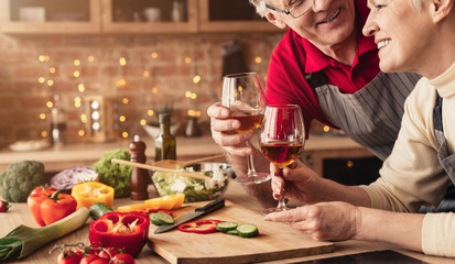 Happy retired man and woman drinking wine at kitchen