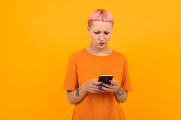 Extraordinary beautiful woman with short pink hair and big tattoo on her hand smiles isolated on orange background