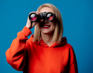 blond girl in hoodie holds binoculars in hand