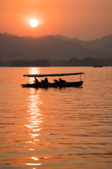 Sunset view of the West Lake in Hangzhou, China. Beautiful silhouette of chinese boats on the lake in sunset colors.