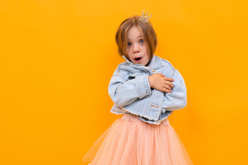 surprised charming beautiful baby girl in a denim jacket and skirt posing on a yellow background with copy space
