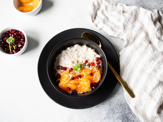 Oatmeal with fresh tangerine slices and pomegranate seeds, ground almonds and mint in a black bowl