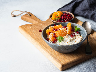 Oatmeal with fresh tangerine slices and pomegranate seeds, ground almonds and mint in a blue bowl on wood board. Copy space.