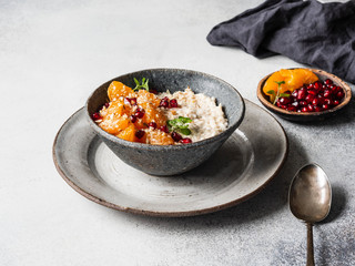 Healthy and tasty breakfast - oatmeal with fresh tangerine slices and pomegranate seeds, ground almonds and mint in a blue bowl on grey background.