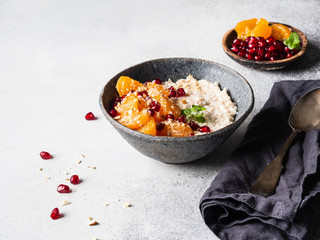 Oatmeal with fresh tangerine slices and pomegranate seeds, ground almonds and mint in a blue bowl on grey background. Copy space