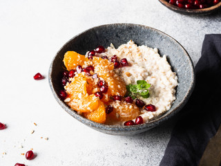 Oatmeal with fresh tangerine slices and pomegranate seeds, ground almonds and mint in a blue bowl on grey background. Copy space