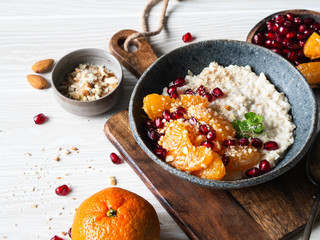 Oatmeal with fresh tangerine slices and pomegranate seeds, ground almonds and mint in a blue bowl on white background.