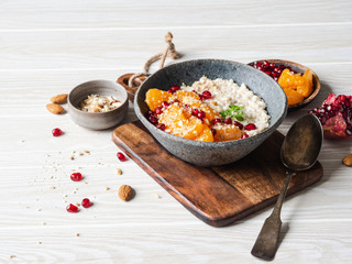 Oatmeal with fresh tangerine slices and pomegranate seeds, ground almonds and mint in a blue bowl on white background. Copy space.