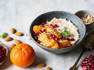 Oatmeal with fresh tangerine slices and pomegranate seeds, ground almonds and mint in a blue bowl on white background.