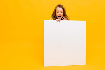 surprised girl holds an advertising poster with a mockup on a yellow background with copy space