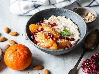 Oatmeal with fresh tangerine slices and pomegranate seeds, ground almonds and mint in a blue bowl on a white background.