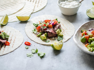 Tortillas with vegetables and beef steak slices. Avocados, tomatoes, red onions and meet with cilantro and lime juice in tortillas. Mexican food.