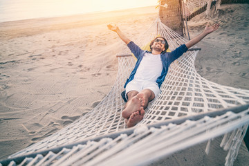 Young man relaxing in hammock on beach. Happiness, freedom of vacation and travel concept. Open arms