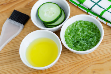 Cucumber and olive oil in a small white ceramic bowls for preparing natural facial mask. Homemade cosmetics recipe