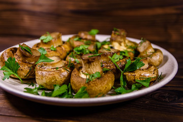 Plate with baked champignons, dill and parsley on a wooden table