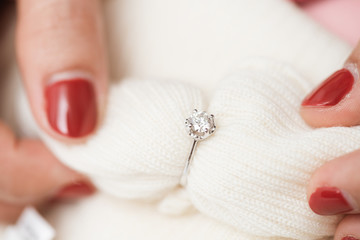 Obraz na płótnie Canvas Close up of an elegant engagement diamond ring on woman finger with pink sweater winter clothe.