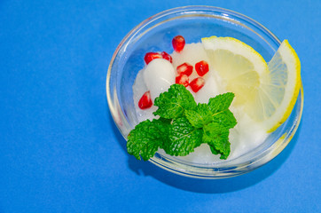White ice cream sorbet with slice of lemon and fresh mint leaves in glass  on blue background, refreshing summer diet dessert, top view copy space.