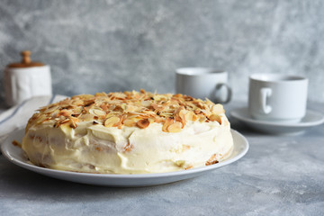Vanilla cake with butter cream, bananas and almonds on a concrete background.