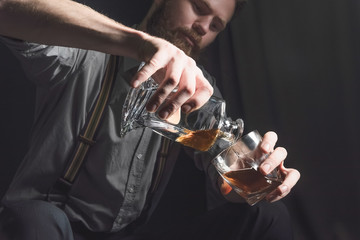 Portrait of a pensive handsome young man, with a glass of alcohol in his hands.