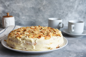 Vanilla cake with butter cream, bananas and almonds on a concrete background.