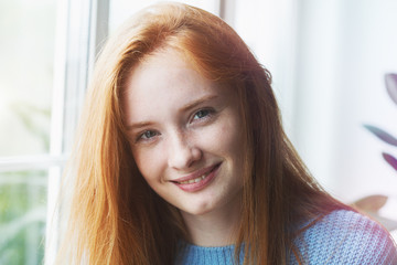 candid indoor portrait of pretty smiling red haired young girl, sunny morning light