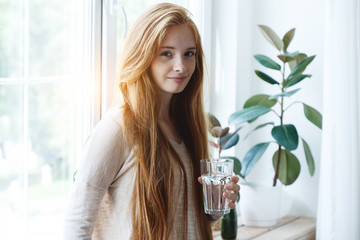 healthy beautiful red haired young woman holding glass of pure water to drink