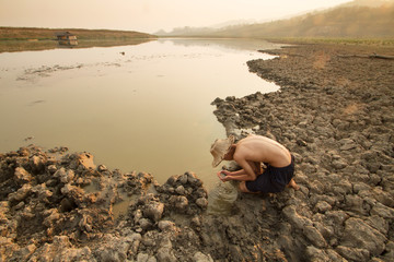 Man taking water from drying pond, river on summer metaphor water crisis and climate change impact.