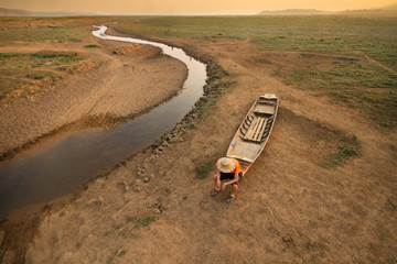 Man sitting on wooden boat at drying river and lake with sadness metaphor Climate change, Water...