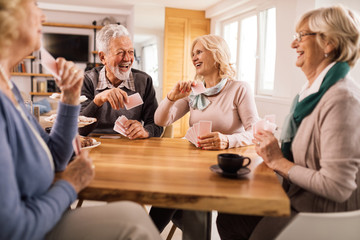 Cheerful senior friends having fun while playing cards together. - obrazy, fototapety, plakaty