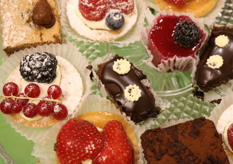 Chocolate and fruit cakes of different sharpness on a glass dish on a green table.