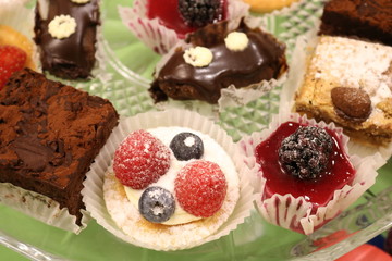 Assorted cakes of different sharpness on a crystal platter on a green table.
