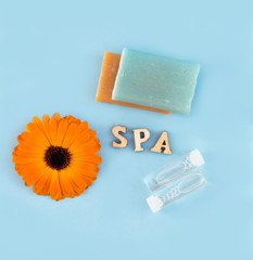 Spa composition. Calendula officinalis plant, bright little soap, Vial with extract. The inscription in wooden letters -SPA. The concept of health and cosmetology.flat lay. Blue background.