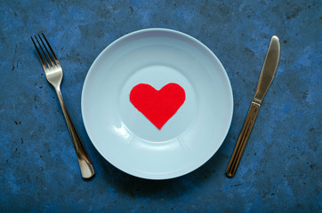 flatlay cute composition red rag heart in a blue plate with a knife and a fork on the sides on a dark blue background. happy birthday or happy valentines day or other universal greetings.