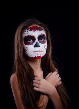 Little beautiful girl with a sugar skull makeup a on a dark background.  Dia de los muertos. Day of The Dead. Halloween costume and make-up.