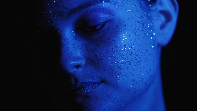 Glitter portrait. Fashion alien. Mysterious woman with shimmering face in neon blue light.