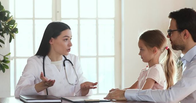 Professional female pediatrician talking with cute child girl and dad