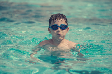 The portrait of the cute European boy in swimming goggles in hotel’s swimming pool. He is enjoying his summer holidays.
