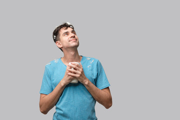 Young brunet man with white feather from a pillow holding white cup with coffee