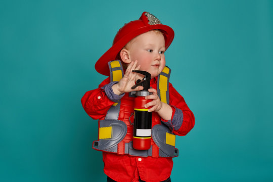 A little boy in a fireman costume plays and dreams of putting out the fire. Fireman on a blue background.