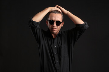 Obraz premium Confident stylish man in black eyeglasses fixing hair isolated over black background.