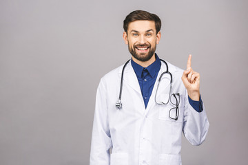 Portrait of cheerful smiling young doctor with stethoscope over neck in medical coat standing against isolated gray background.