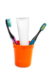 Plastic cup with toothbrushes and tube of toothpaste on white.
