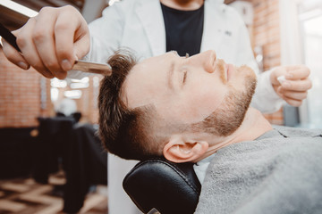 Hairdresser barber is holding razor for beard, male client is sitting in chair